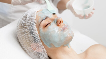 A cosmetologist applies an alginate face mask on a young woman in a modern salon. This treatment boosts skin hydration and rejuvenation, perfect for highlighting premium skincare in your ads.