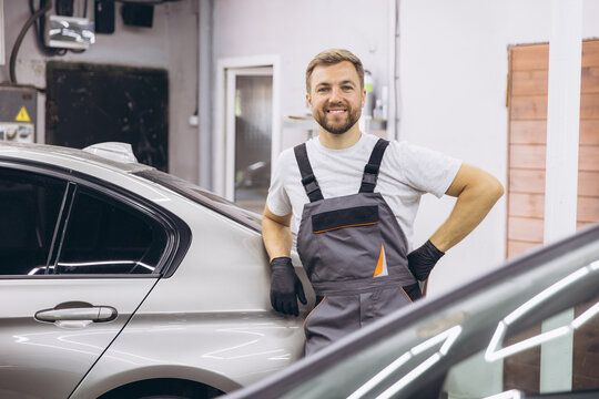 Smiling Auto Mechanic Standing Confidently Beside Silver Car in Garage Workshop