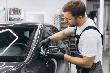 Professional Auto Mechanic Applying Protective Film to Car Mirror in Workshop