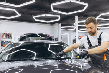 Man washing car hood and preparing the polishing process Car glass coating. Male worker installing protection film to car in garage. Car Detailing.