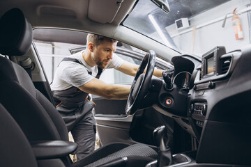 A mechanic's shop worker sitting in a car and checking on steering wheel on a car service.