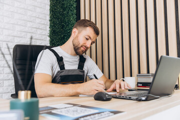 Caucasian business manager or mechanic sitting and writing report in front of laptop-notebook in office at car service