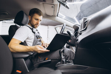 Automotive mechanic running diagnostics software on computer. Mechanic sitting in car and working on laptop while doing vehicle diagnostic test in auto service garage.