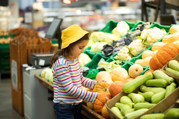 Kid little cute girl shopping for fresh organic fruits and vegetables in supermarket. Little girl holding pumpkin in a hands.