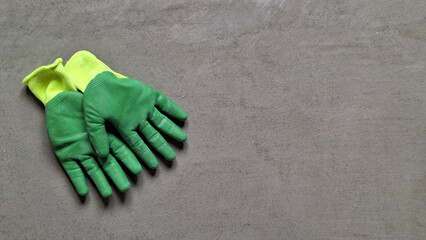 Yellow and green work gloves lie on a flat concrete surface. Background. Texture. There is space for text.
