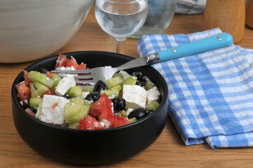 Salade grecque faite maison dans un ramequin noir avec une fourchette servie avec un verre d'eau en gros plan.