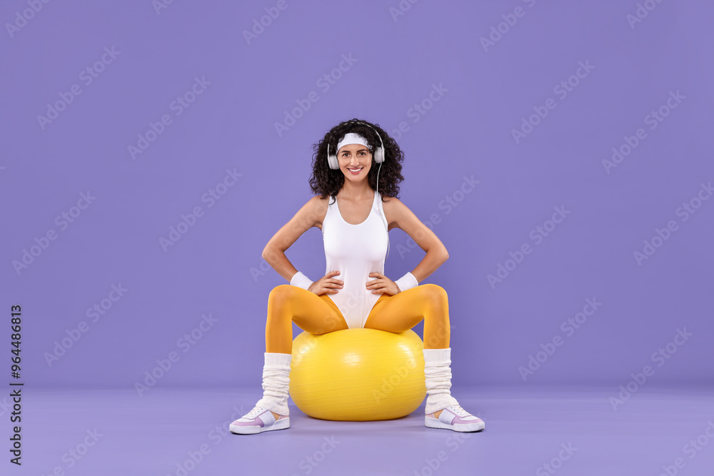 Poster Woman in headphones doing aerobic exercise with dumbbells and fitness ball on purple background