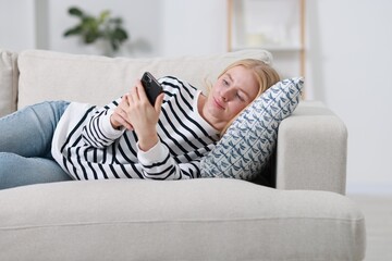 Fototapeta premium Beautiful woman using smartphone on sofa indoors