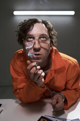 Man wearing glasses in orange suit, holding key, and smoking with deep thought-filled expression....