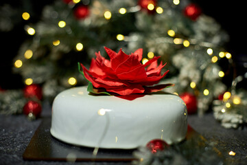 A beautifully crafted dessert showcases a striking flower decoration, enhanced by twinkling lights and festive greens, creating an inviting holiday atmosphere.