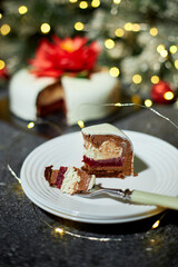 A beautifully arranged plate holds a slice of decadent layered cake, showcasing red velvet and cream cheese layers, surrounded by twinkling lights and holiday decor.