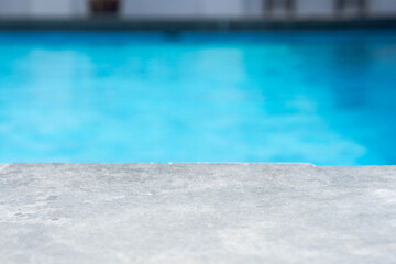Empty grey ceramic table top and blurred swimming pool in tropical resort in summer banner background