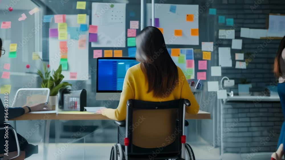 Poster woman in a wheelchair working at a desk in an office with colorful sticky notes on a glass wall. inc