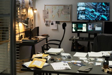 Dimly lit office with multiple monitors and crime scene photos scattered around. Desk cluttered...