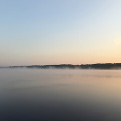 Fototapeta premium Serene Lake at Dawn with Morning Mist Rising Over Calm Water