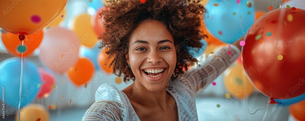 Wall mural A woman with a joyful expression, holding colorful balloons and jumping in celebration against a plain white background.