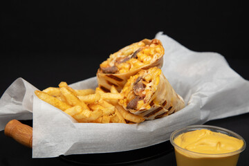 Savory Burrito Wrap with French Fries and Cheese Sauce: Mexican-Inspired Fast Food Meal on White Paper, Black Background, Wooden Handle Knife.