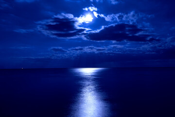 Sky is dark and the moon is shining brightly over the ocean. Moon illuminates the ocean under a clear blue sky, creating a serene and tranquil nighttime scene