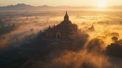 Aerial view of the ancient temples of Bagan at sunrise, with mist hanging low over the landscape.