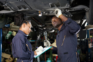 African mechanic workers fixing underneath car and talking about work in garage