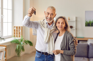 Portrait of a smiling elderly family couple is celebrating the purchase of new home together. They are showing the keys to their new house, expressing happiness and joy about new property ownership.