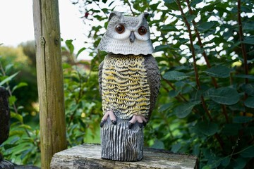 Big grey white yellow plastic owl figure or statuette in front of green background. Big brown eyes.