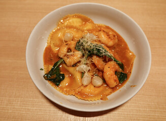 close up of Italian lobster sauce prawns shrimp stuffed ravioli with herbs on a white bowl