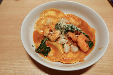 close up of Italian lobster sauce prawns shrimp stuffed ravioli with herbs on a white bowl