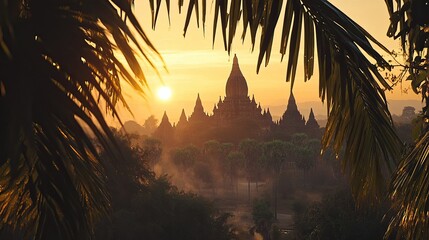 The ancient temples of Bagan seen through a frame of palm trees, with the sun setting in the background.