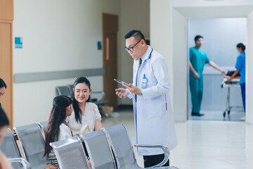 Fototapeta premium Happy asian male doctor with digital tablet examining child patient with mother in hospital
