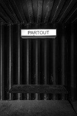 Waiting bench in black tin against an industrial background with a luminous sign above it with French text "partout" (everywhere)