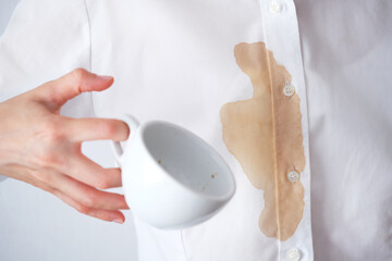 Unrecognizable person in a light white shirt spills coffee on themselves while holding a white cup...
