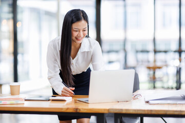 Asian Businesswoman Using laptop computer and working at office with calculator document on desk, doing planning analyzing the financial report, business plan investment, finance analysis concept.
