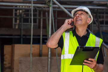 Male Builder Construction Worker on Building Site With Clipboard and Cell Phone