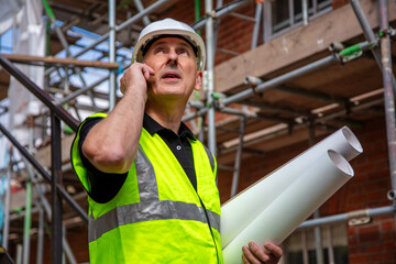 Male Builder Construction Worker Architect on Building Site Using Phone and Plans