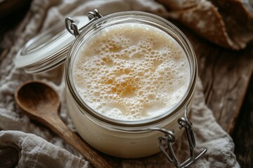 Close-Up of Artisan Homemade Sourdough Starter in Clip-Lid Food Preservation Jar with Rustic Wooden Spoon and Linen Cloth on Wooden Table Professional Artisan Food