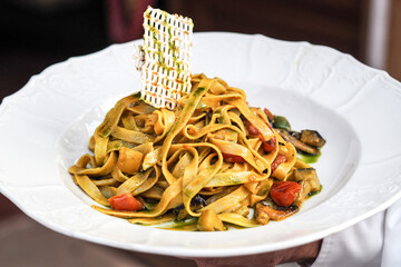A gourmet plate of tagliatelle pasta topped with roasted vegetables and a delicate crisp, served in a Jewish fine dining restaurant. The vibrant presentation highlights elegant culinary artistry.