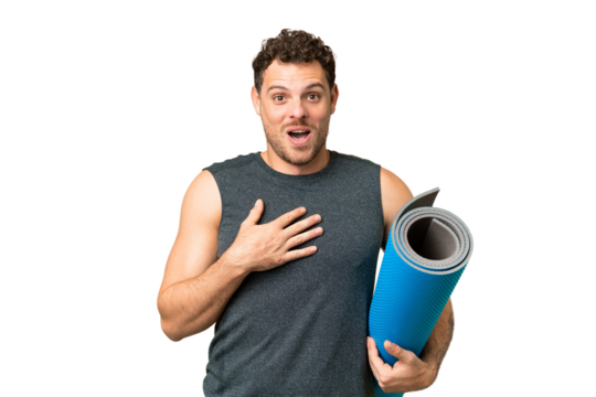 Young sport man going to yoga classes while holding a mat over isolated chroma key background surprised and shocked while looking right