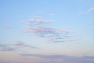 Bright blue sky with clouds lit by early morning sunshine. Blue, white, purple, and orange. Nice sky background