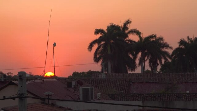 The sun on the horizon over rooftops with palm trees in tropical Nicaragua