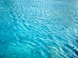 Blue water ripple texture on open vast ocean, with different shades of blue, dark blue, and light blue from sea base. Beautiful water ripple wave reflecting the sun lights.