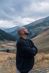 A thoughtful bald man, arms crossed, gazes up at the sky with his head held high against the...