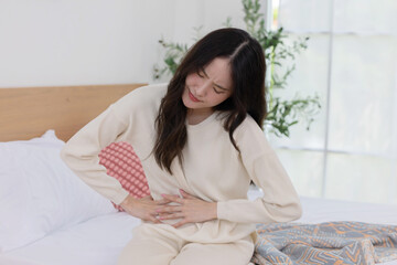 Asian woman grab her stomach suffer from stomach ache on her bed