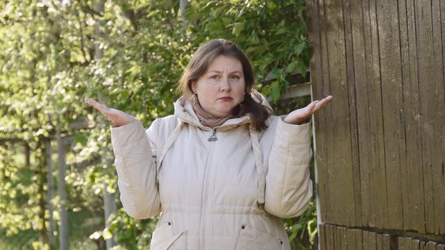 Portrait of middle aged woman who cant make choice. Caucasian woman shrugs her shoulders in doubt and shakes her head negatively, raising both hands up outdoors.