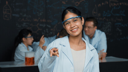 Highschool girl looking at camera while people doing experiment at laboratory. Young cute student...