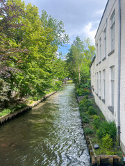 Brugge, Flanders, Belgium - June 22, 2024: Sint-Janskaai canal seen from Zonnekemeers bridge and view of Beguinage bridge among gree foliage trees. White facade on right