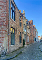 Brugge, Flanders, Belgium - June 23, 2024: Twijnstraat, street, from corner of Middelburgstraat under blue sky. Facade row of residential houses