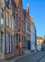 Brugge, Flanders, Belgium - June 23, 2024: Twijnstraat, street, from corner of Middelburgstraat under blue sky. Facade row of residential houses
