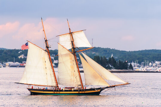 A two-masted schooner sailing at sunset under full sail along the coast of Maine