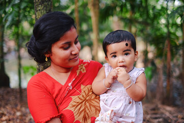 Obraz premium South asian rural young mother holding and watching her little baby girl with love and care, family togetherness concept 